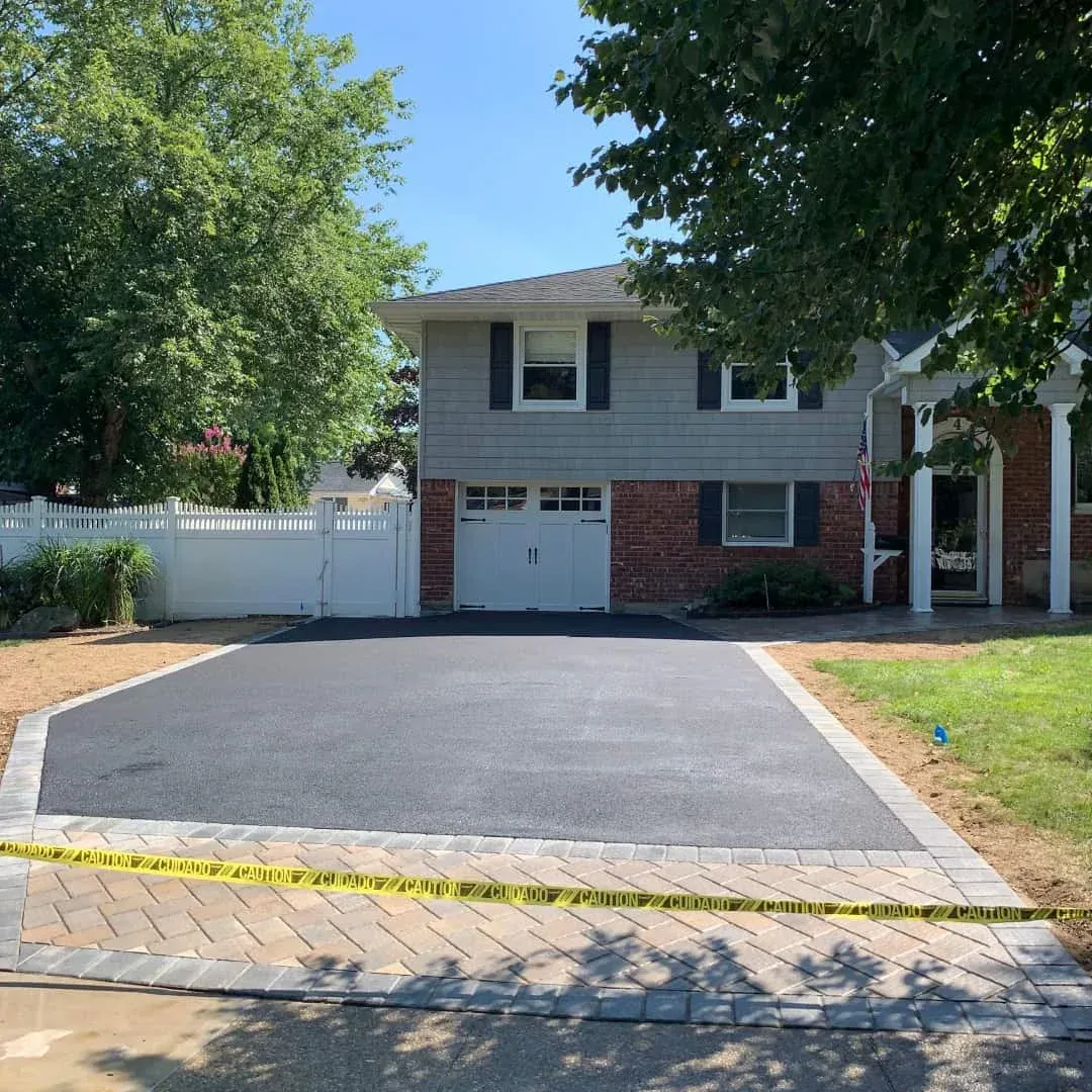 Suburban house with a newly paved black driveway bordered by yellow caution tape