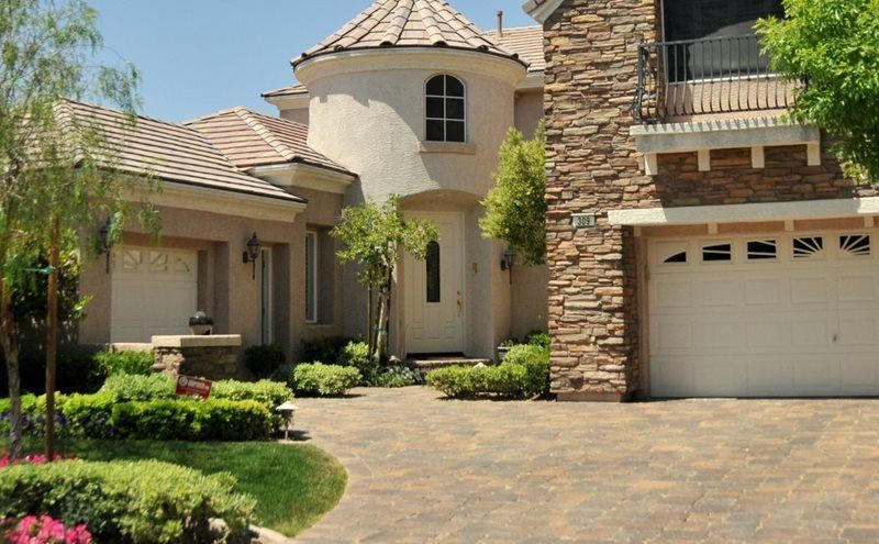 Large stucco house with stone accents, arched entry, and a garage, viewed from the driveway