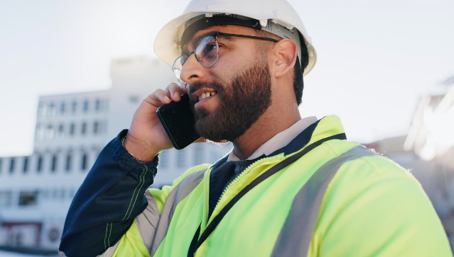 Construction worker in yellow vest and hard hat talking on a cellphone outdoors