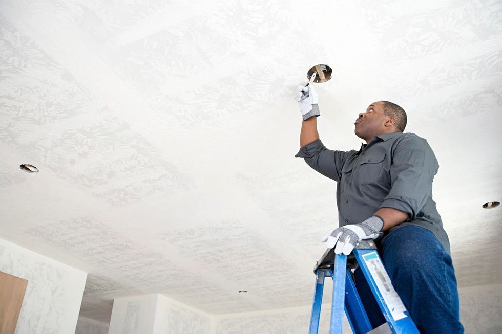 Person on a ladder working on a ceiling electrical fixture; wearing work gloves.