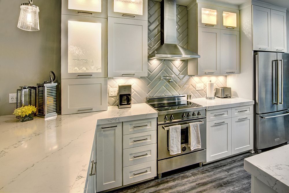 Modern white kitchen with stainless steel appliances, herringbone backsplash, and quartz countertops.