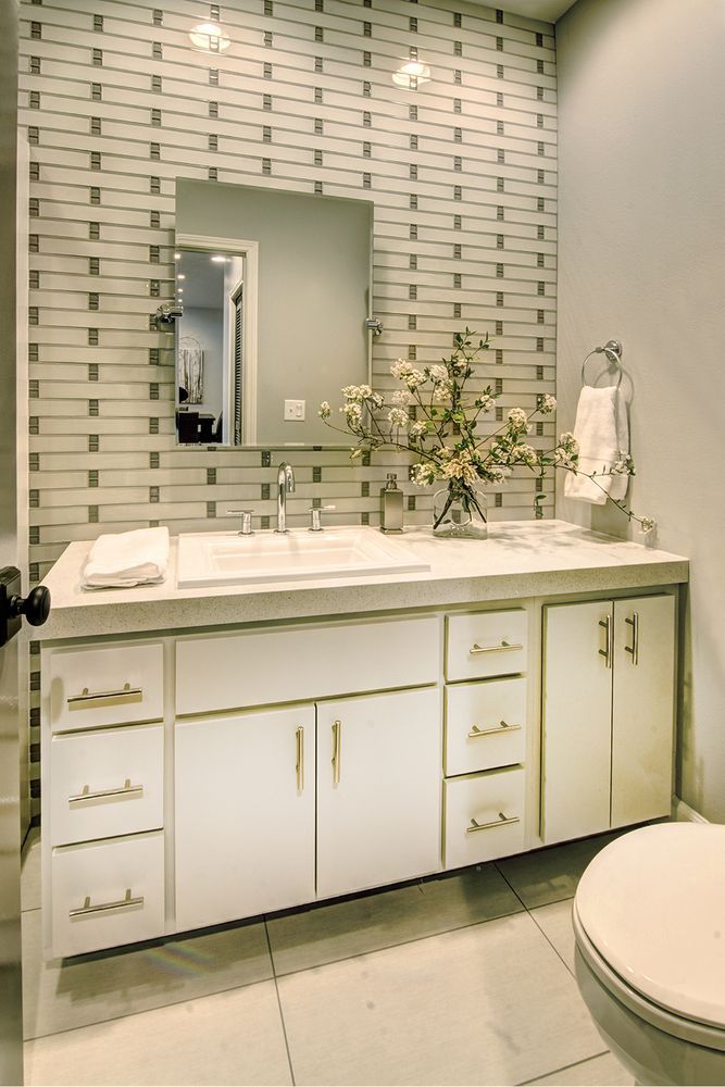 White bathroom with vanity, mirror, patterned wall, and toilet.