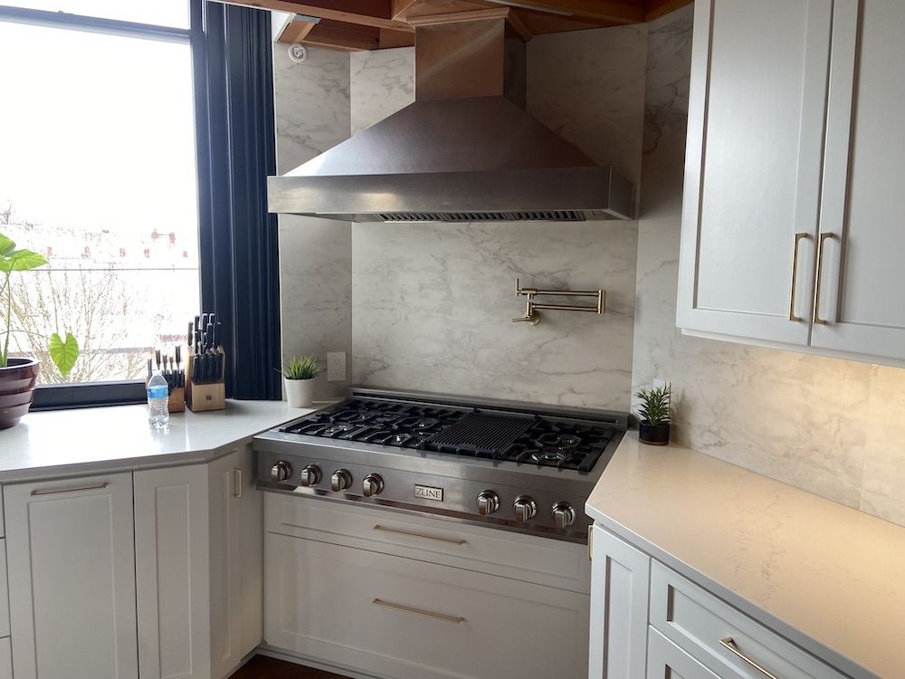 Stainless steel range and hood in a modern white kitchen.
