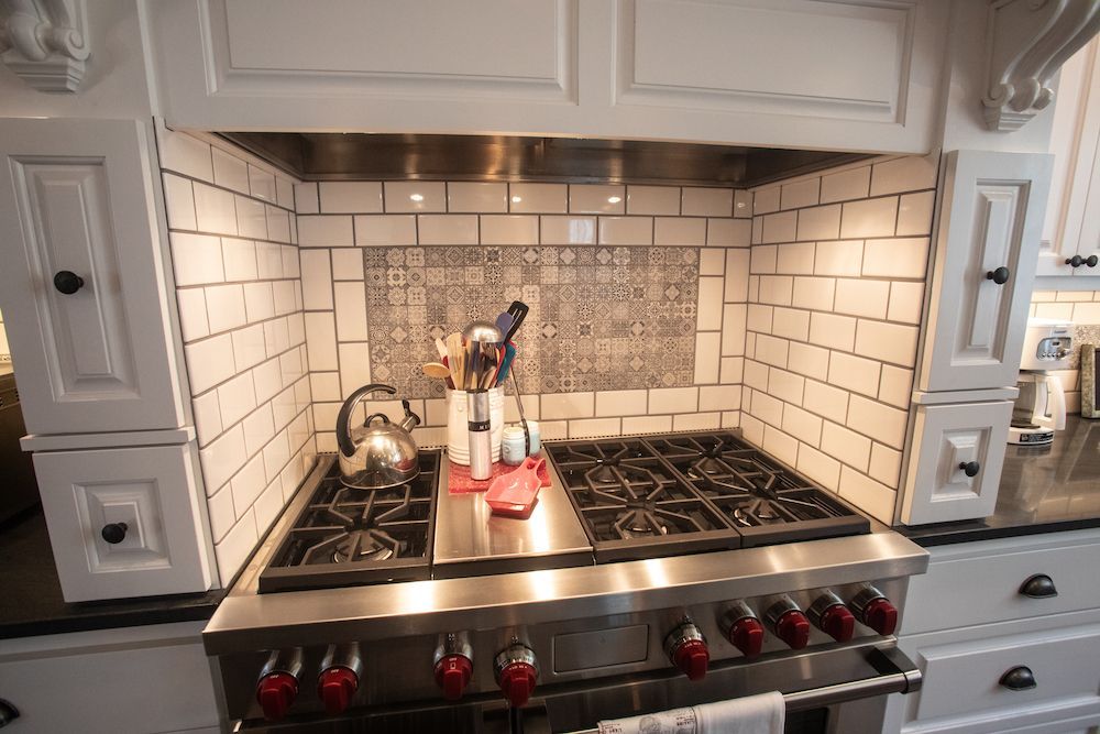 Kitchen stove with white subway tile backsplash, stainless steel hood, and black countertops.