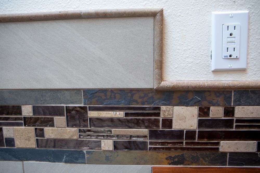 Wall with decorative tile and an electrical outlet.