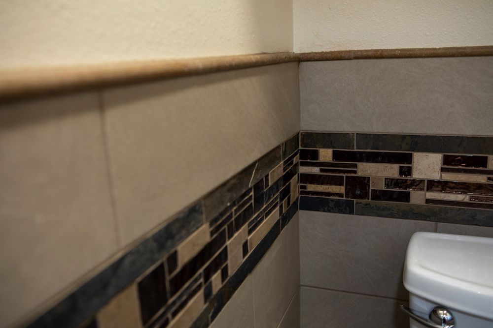 Bathroom corner with tiled walls, beige and mosaic accent, toilet partially visible.