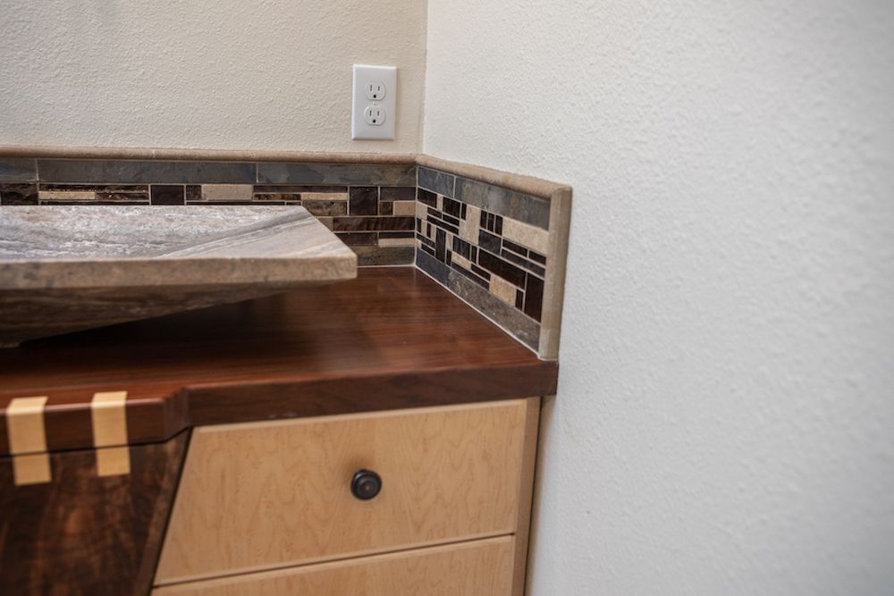 Bathroom vanity with wood countertop, mosaic tile backsplash, and light-colored cabinet.