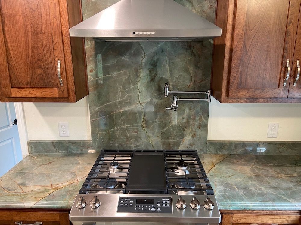 Kitchen with stainless steel range, hood, and green stone backsplash. Dark wood cabinets.