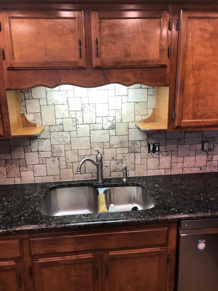 Kitchen with a stainless steel sink, dark granite countertop, brown cabinets, and a tile backsplash.