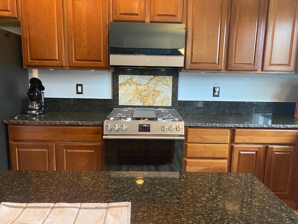 Kitchen with brown cabinets, stove, and granite countertops. Blue wall, decorative backsplash.