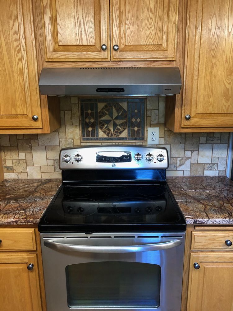 Stainless steel stove in a kitchen with wooden cabinets and a stone backsplash.