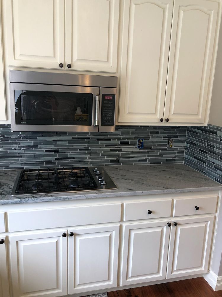 Kitchen with white cabinets, stainless steel microwave, gas stovetop, and blue tile backsplash.