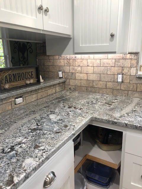 Kitchen with granite countertops, brick-like backsplash, white cabinets, and an open cabinet.