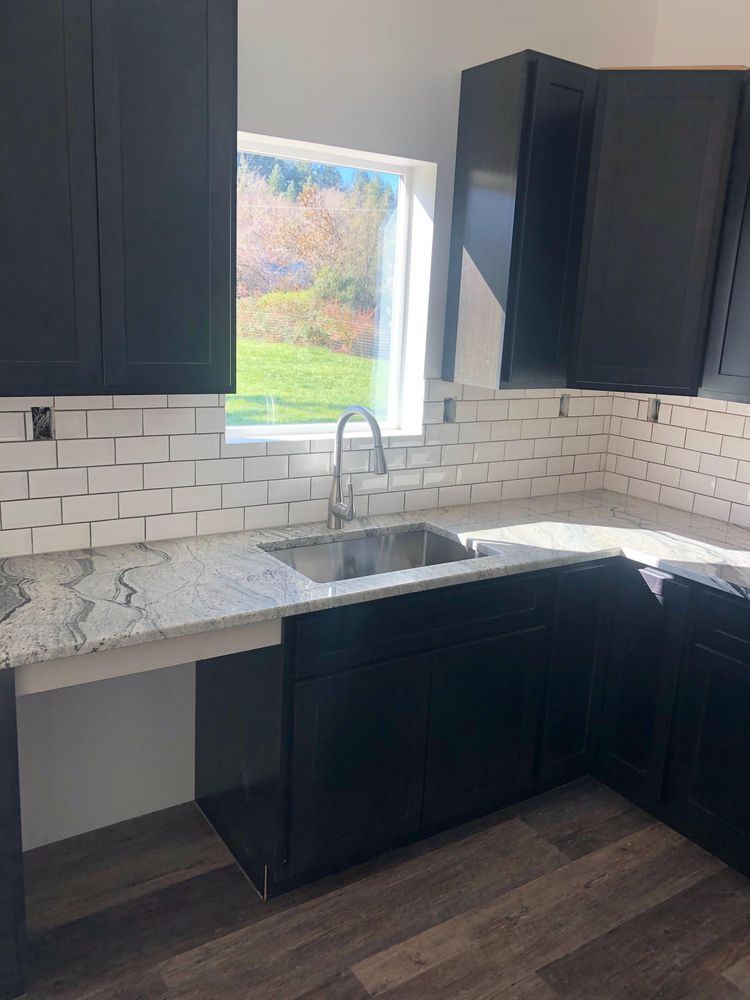 Kitchen with black cabinets, white backsplash, granite countertop, and accessible sink area.