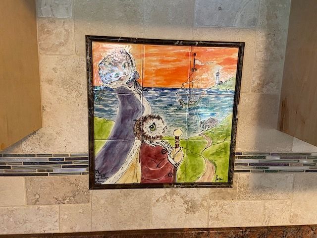 Painted tiles with a figure, owl, and golf scene. Orange sky, blue sea, green hills.