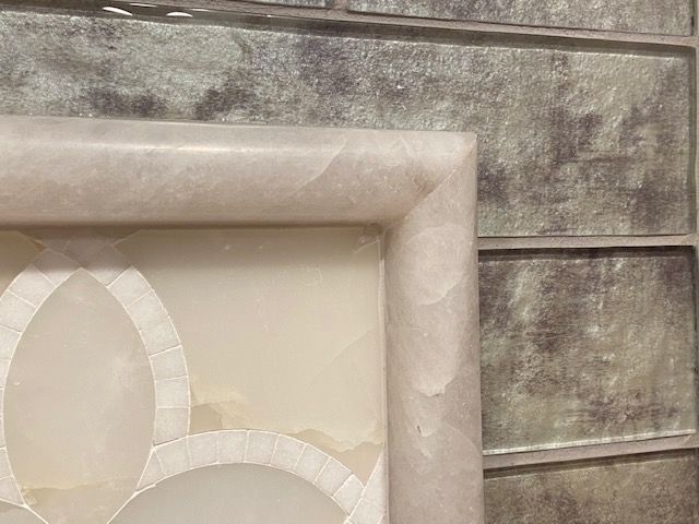 Close-up of a framed, light-colored design against a textured, gray-brown tiled wall.