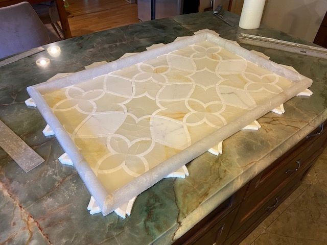 Marble tile mosaic with floral pattern inside a raised border on a stone countertop.