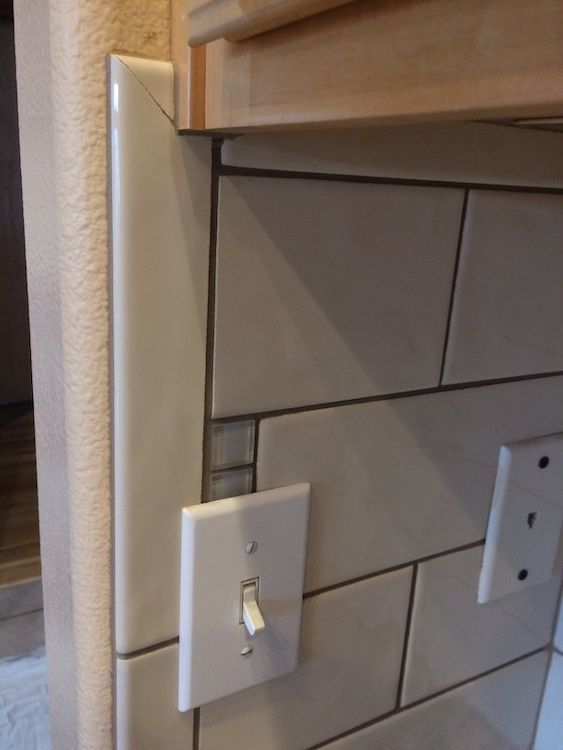 Close-up of a kitchen wall with beige tiles, a light switch, and a beige decorative tile border.