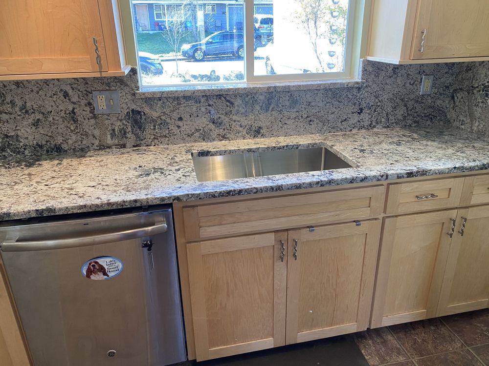 Kitchen with stainless steel sink, light granite countertop, light wood cabinets, and a dishwasher.