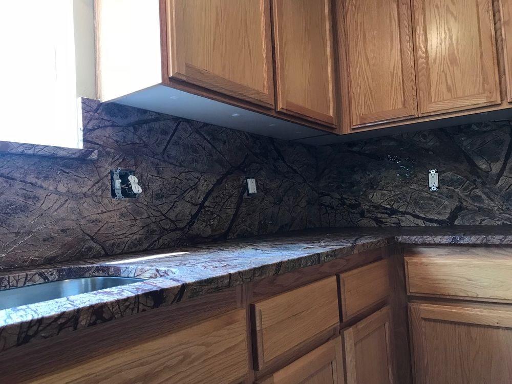Kitchen countertop and backsplash with brown and tan granite, under wooden cabinets.