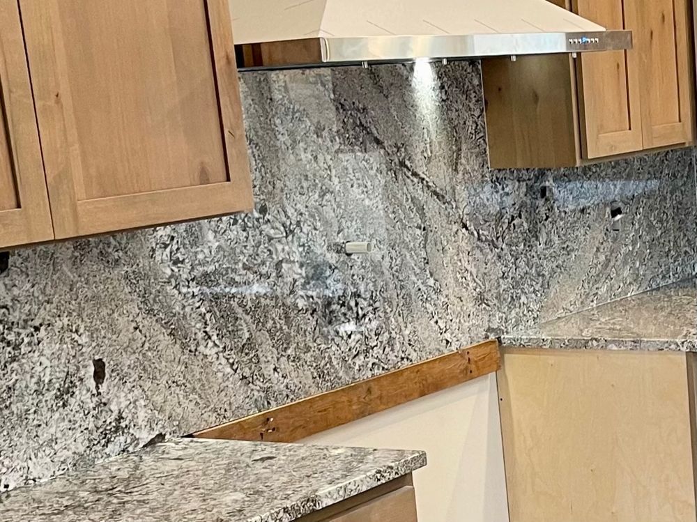 Kitchen with light wood cabinets, granite countertops, and patterned backsplash behind the stove.