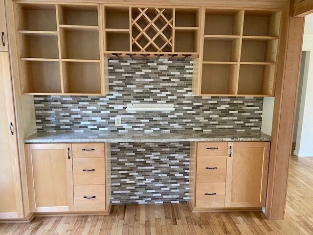 Built-in wooden cabinet with shelves, wine rack, and countertop with tile backsplash.