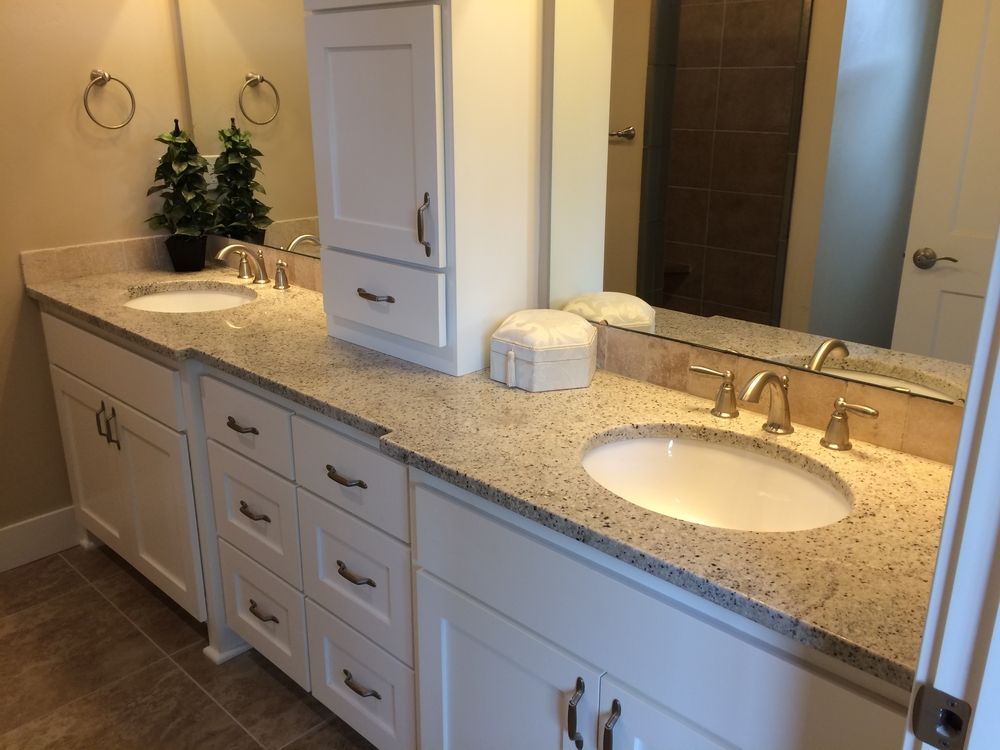 Bathroom with dual sinks, white cabinets, speckled countertop, large mirror, and neutral-colored walls.