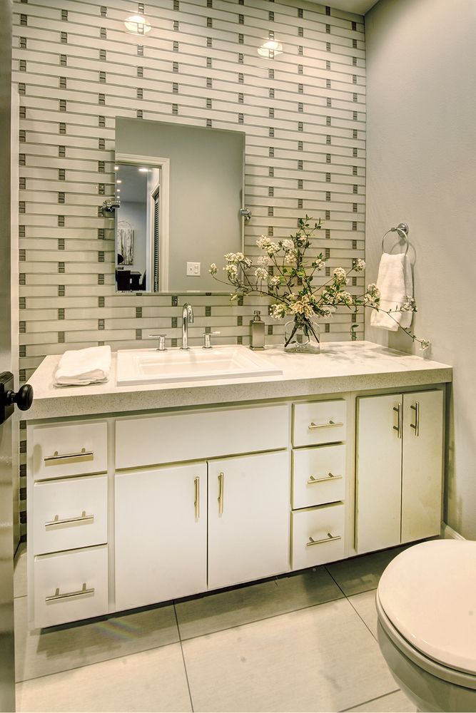 White bathroom with a white vanity, gold hardware, and patterned tile backsplash.