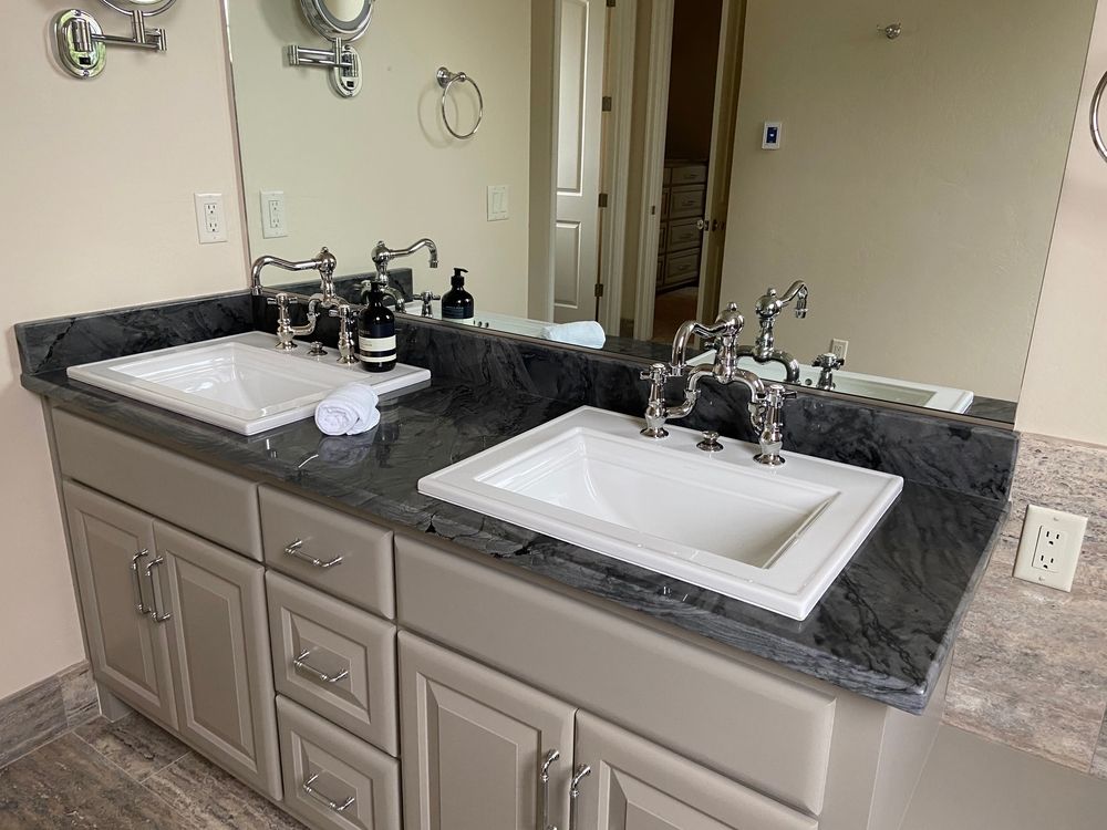 Bathroom vanity with two sinks, gray cabinets, gray countertop, and silver fixtures. Mirror reflects the room.
