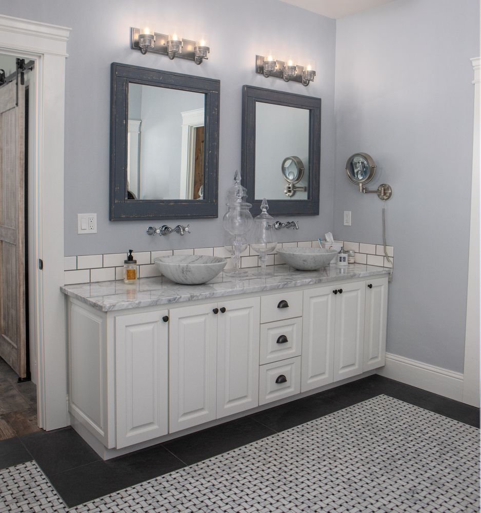 Bathroom with white cabinets, marble countertop, two mirrors, and gray walls.