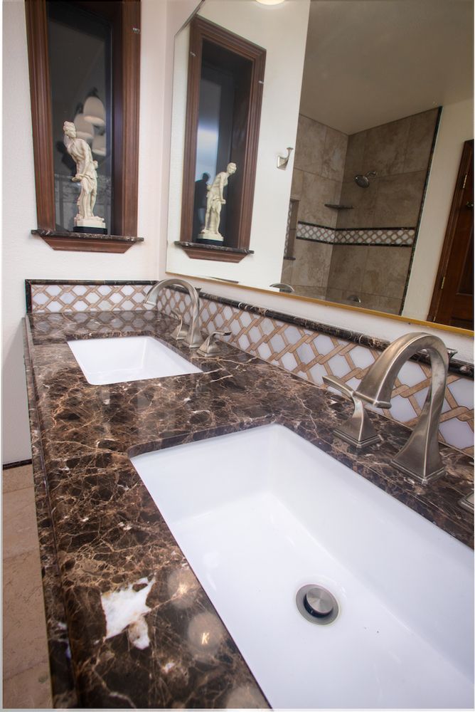 Bathroom with brown marble countertop, white sinks, silver faucets, and mosaic tile backsplash.