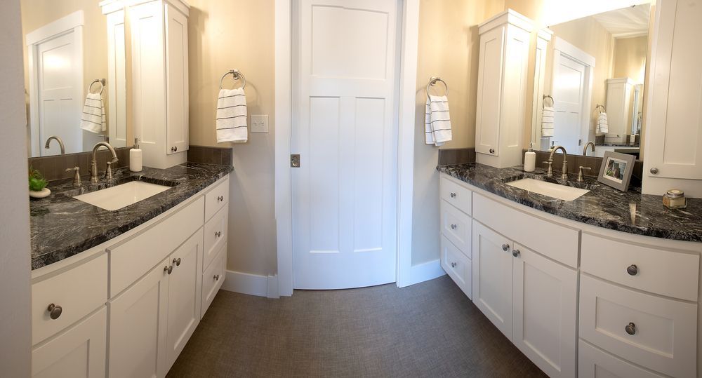 Bathroom with two white vanities, granite countertops, and a white door.
