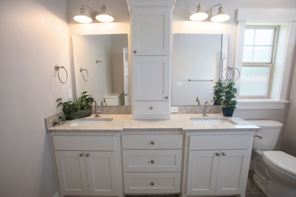 Bathroom with white double vanity, large mirror, and central cabinet.