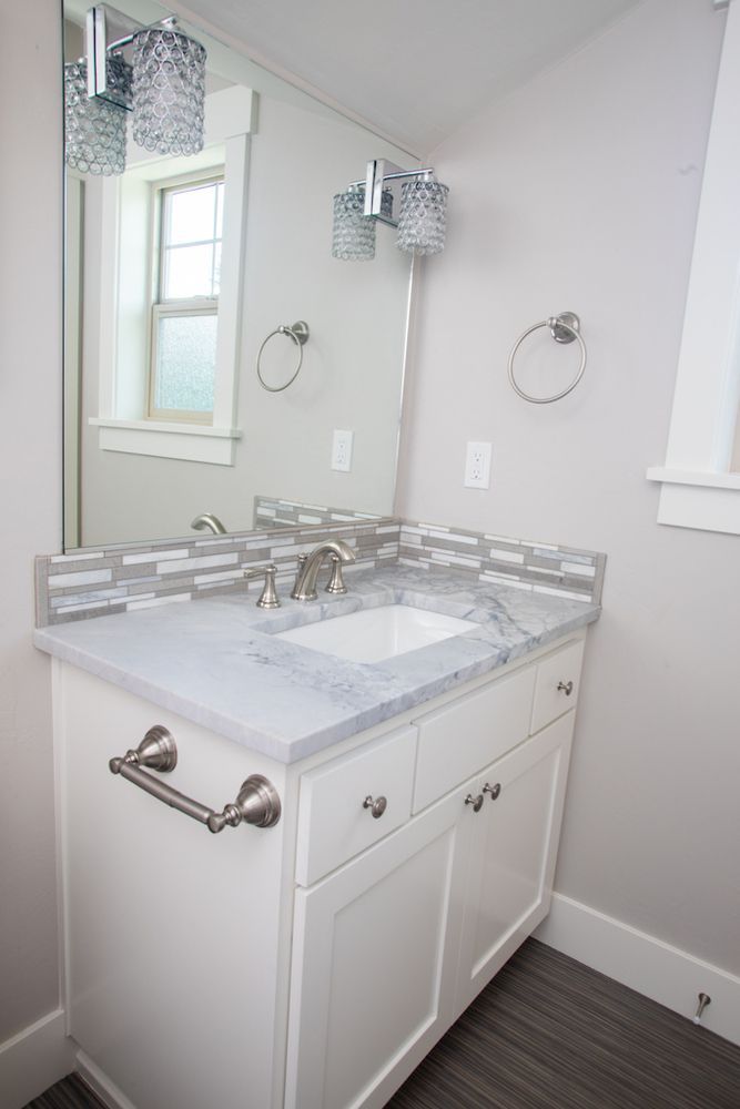 White bathroom vanity with marble countertop, mirror, and silver fixtures.