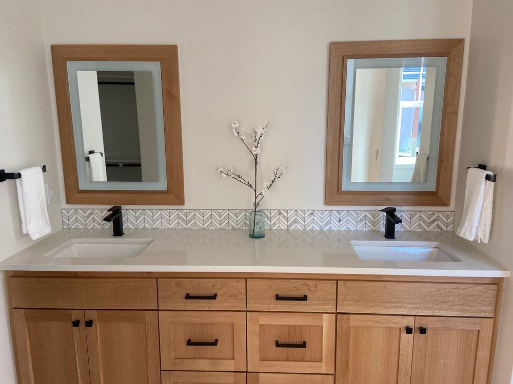 Bathroom vanity with two sinks, light wood cabinets, mirrors, and black faucets.