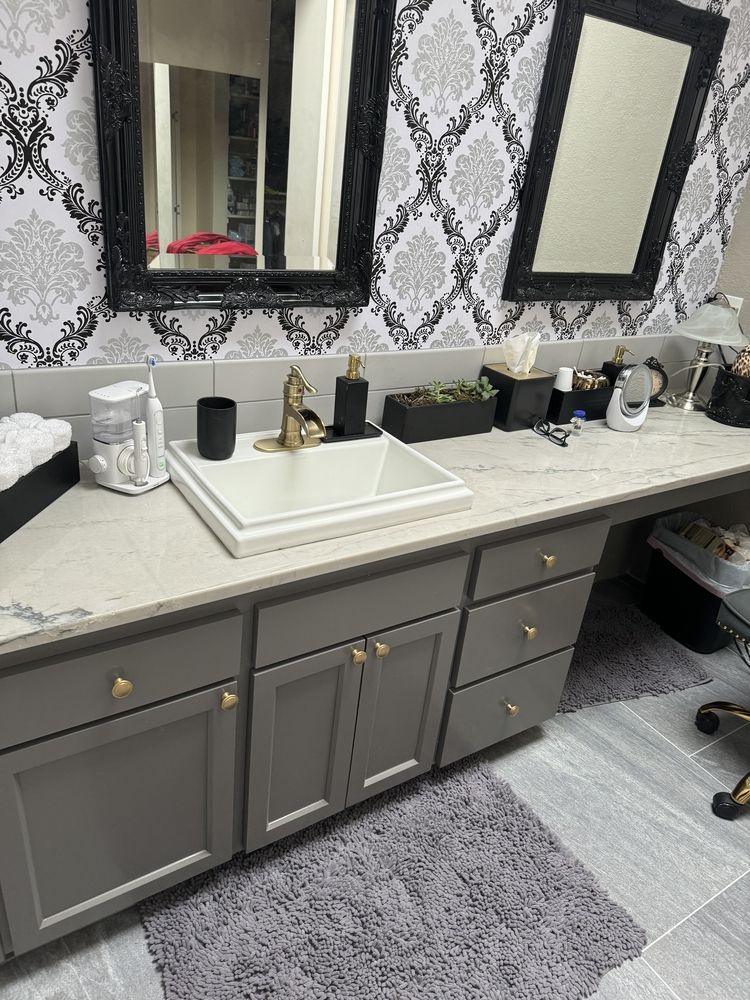 Bathroom with gray cabinets, white sink, decorative wallpaper, and black-framed mirrors.