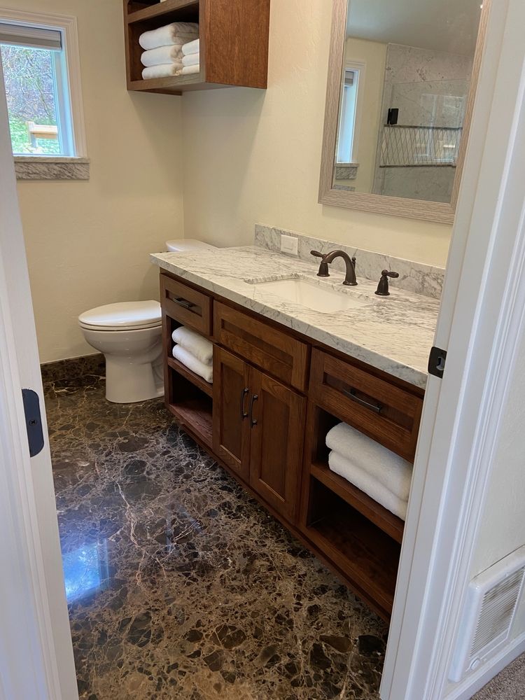 Bathroom with dark patterned floor, wood vanity, white countertop, and stacked towels.