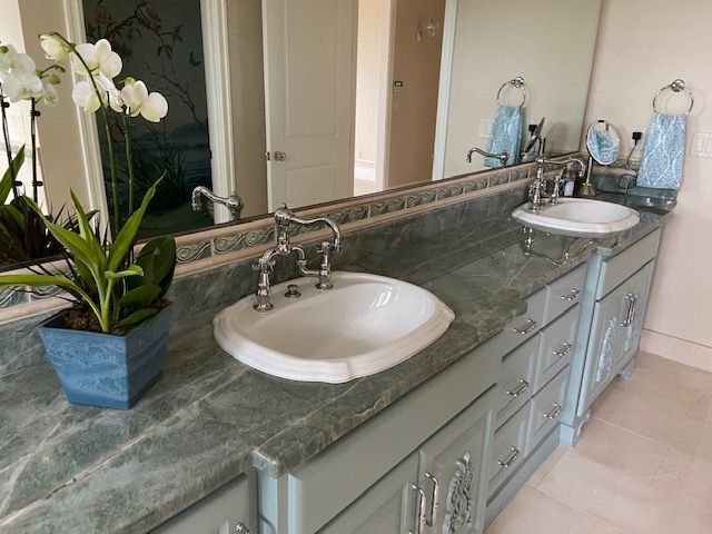 Bathroom with green marble countertop, two white sinks, and gray cabinets. Mirror reflects a doorway.
