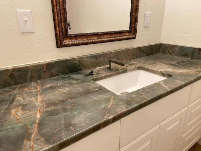 Bathroom vanity with green marble countertop, white cabinets, and framed mirror.