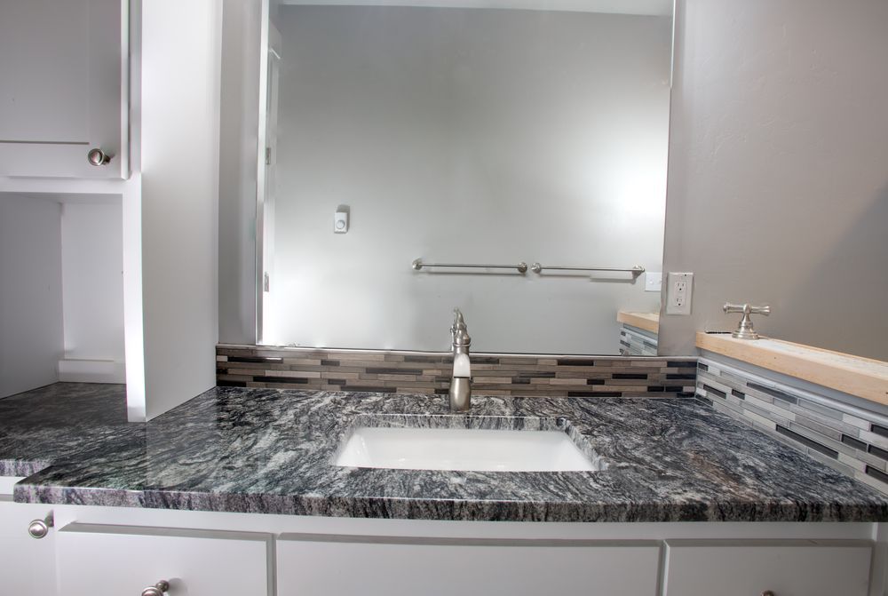 Bathroom vanity with granite countertop, square sink, and large mirror.