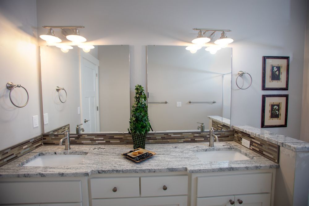 Bathroom with white cabinets, granite countertop, two sinks, mirrors, and wall sconces.