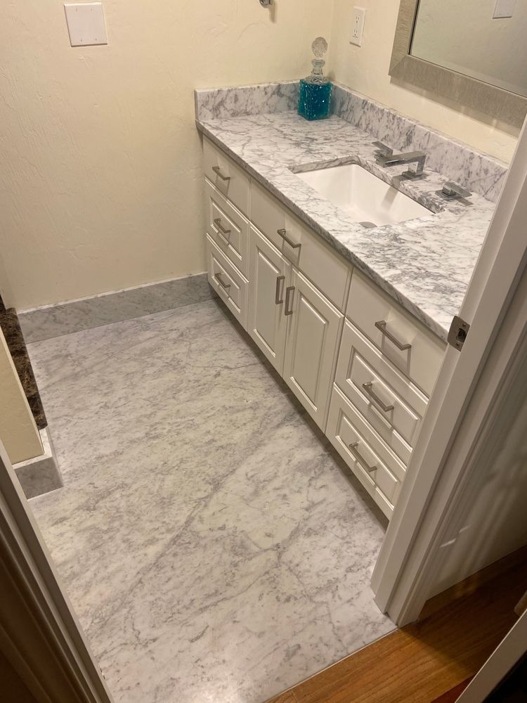 White vanity with granite countertop and sink in a bathroom with marbled flooring.