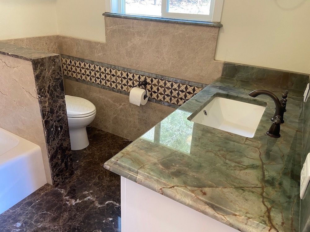Bathroom with granite countertop and sink. Toilet behind a half wall with patterned tile detail.