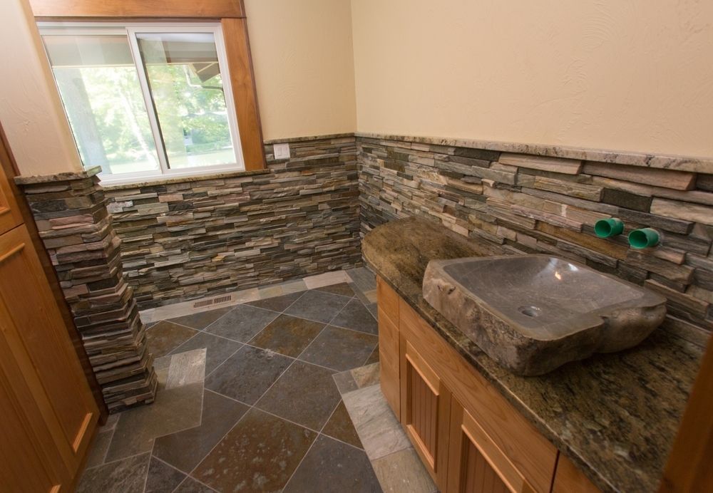 Bathroom with stone tile walls, wooden cabinets, and a stone sink.