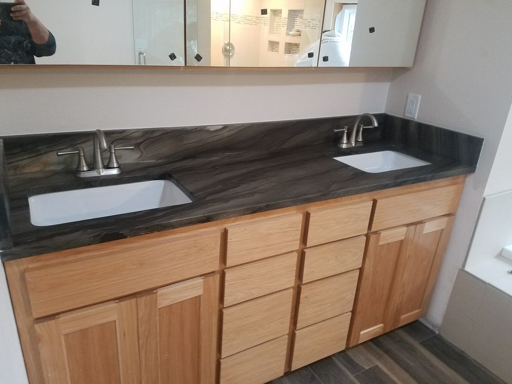 Bathroom vanity with light wood cabinets, dark countertop, and two white sinks.