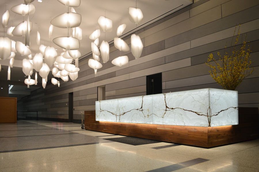 Reception desk with illuminated marble top, wooden base, under a modern light fixture in a modern lobby.