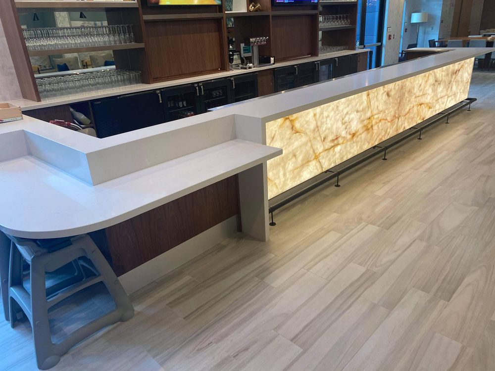 Long illuminated bar with white countertop and wood accents in a modern setting.