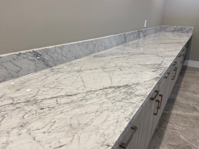 Long, marble-topped countertop with gray veining, set on a light gray cabinet with multiple drawers and bronze handles.