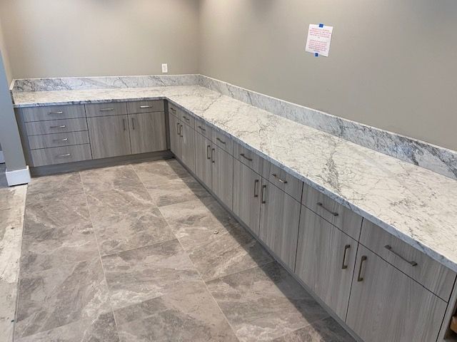 L-shaped light wood cabinets with marble countertops and gray tile floor.