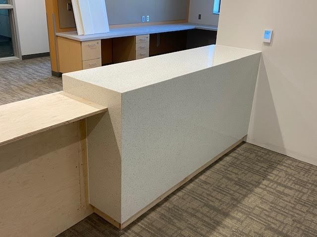 White countertop with speckled surface; beige wood framing; carpeted floor.